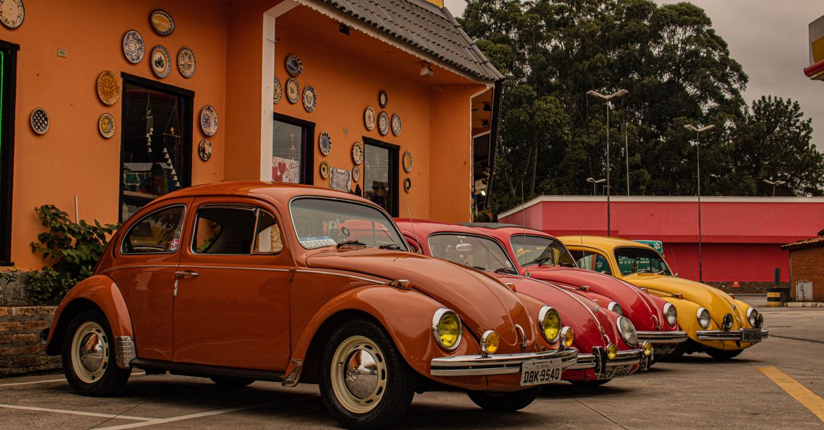 A row of colorful vintage Beetle cars parked beside an orange building, showcasing classic automotive design.